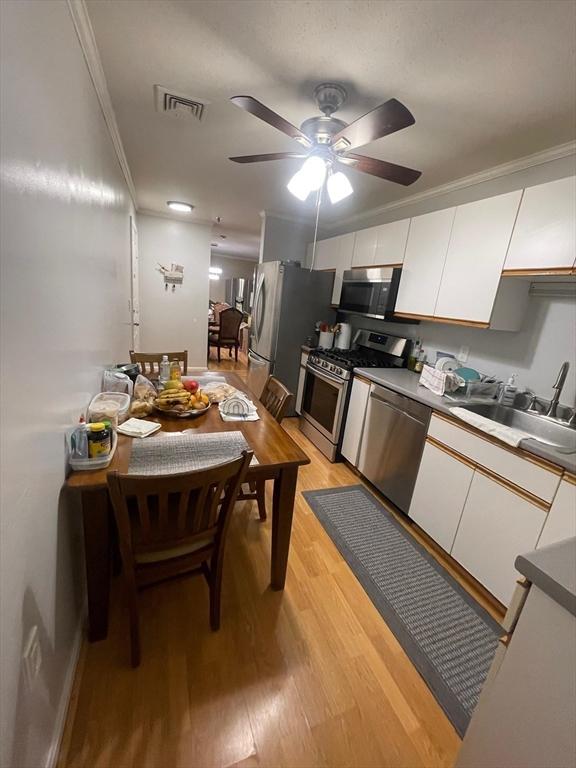 13 Dallas Dr Unit 308, Dracut, MA 01826 - kitchen with appliances with stainless steel finishes, white cabinetry, light wood-type flooring, a ceiling fan, and ornamental molding