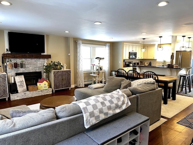 living room with hardwood / wood-style flooring, a brick fireplace, and a baseboard heating unit