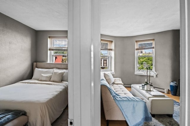 34 Beacon St Unit 3, Chelsea, MA 02150 - bedroom featuring multiple windows, a textured ceiling, a textured wall, wood finished floors, and a baseboard heating unit