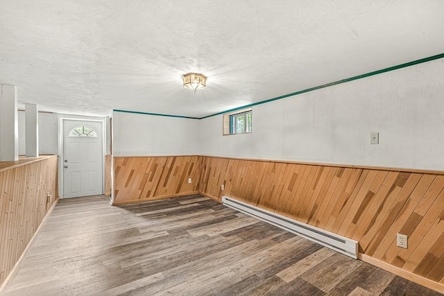 191 Franklin St Unit A, Stoneham, MA 02180 - spare room with a baseboard heating unit, wooden walls, wood finished floors, a textured ceiling, and a wainscoted wall