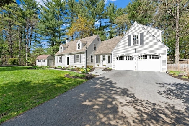 cape cod home featuring fence, aphalt driveway, a storage shed, a front yard, and an outbuilding