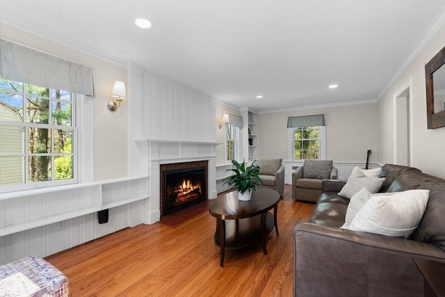 living area with ornamental molding, built in features, a brick fireplace, recessed lighting, and light wood finished floors