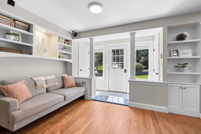 living room featuring built in features, baseboards, ornate columns, and light wood-style flooring