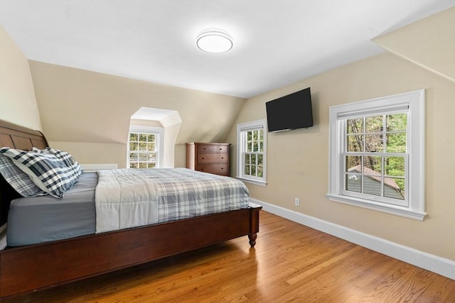 bedroom with baseboards, multiple windows, wood finished floors, and lofted ceiling
