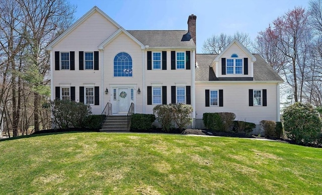 colonial home featuring a front yard, a shingled roof, and a chimney
