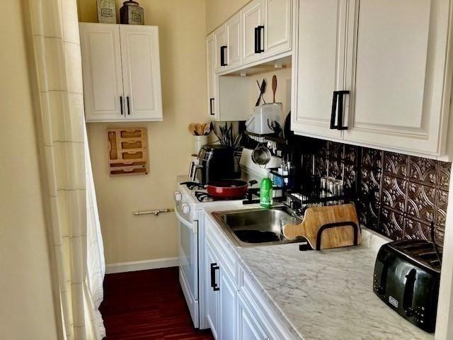 kitchen featuring white gas range, light stone countertops, and white cabinets