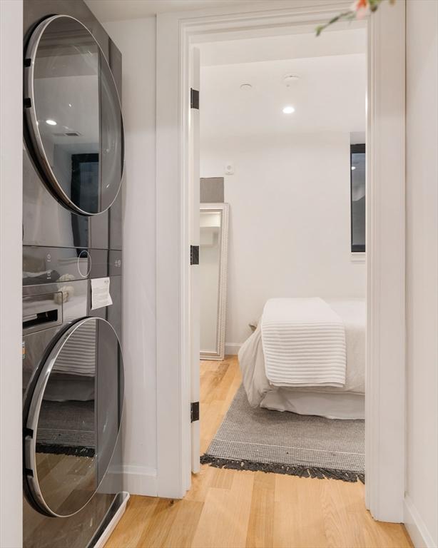 clothes washing area featuring stacked washer and clothes dryer and light wood-type flooring