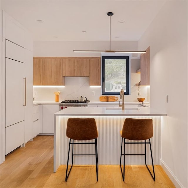 kitchen with sink, light wood-type flooring, white cabinets, pendant lighting, and stove