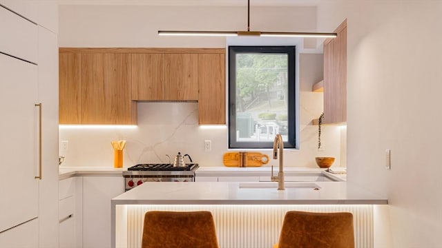 kitchen featuring tasteful backsplash, white cabinetry, sink, and range