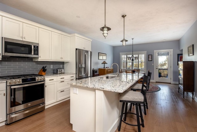 kitchen with decorative light fixtures, sink, stainless steel appliances, and an island with sink