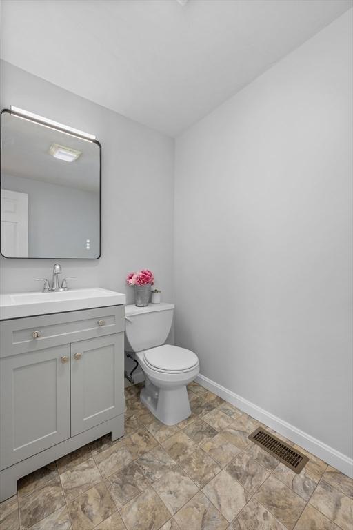 bathroom with toilet, vanity, visible vents, and baseboards