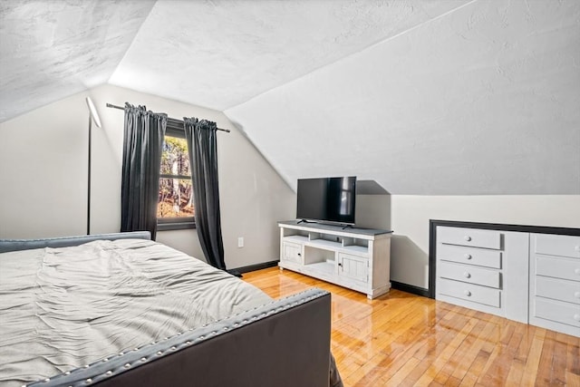 bedroom featuring light wood-style flooring, vaulted ceiling, and baseboards