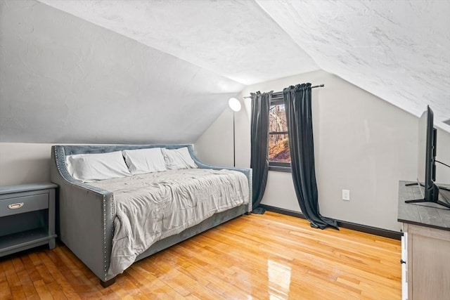 bedroom featuring light wood-type flooring, vaulted ceiling, baseboards, and a textured ceiling