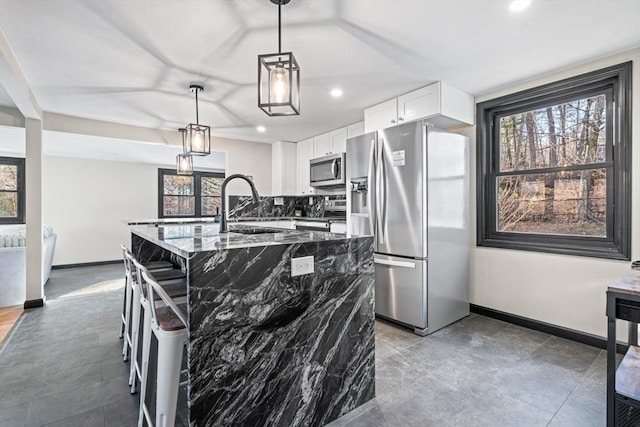 kitchen featuring appliances with stainless steel finishes, a sink, baseboards, dark stone countertops, and white cabinetry