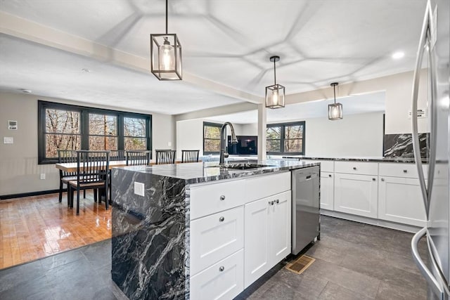 kitchen with stainless steel dishwasher, a sink, dark stone countertops, a kitchen island with sink, and white cabinetry