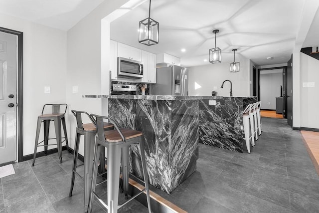 kitchen featuring stainless steel appliances, white cabinetry, a breakfast bar area, dark stone counters, and hanging light fixtures
