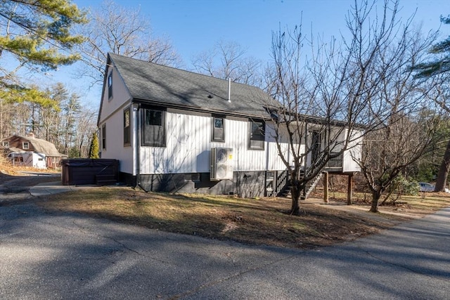 view of property exterior featuring a hot tub, stairway, and a shingled roof