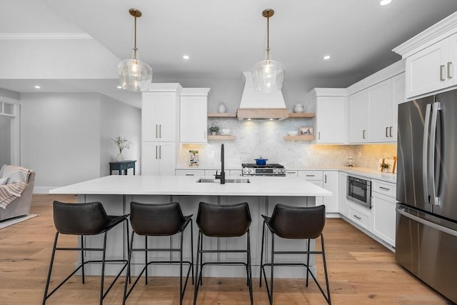 kitchen with custom range hood, stainless steel appliances, light countertops, open shelves, and a sink