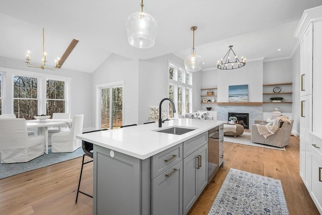 kitchen featuring open floor plan, an inviting chandelier, gray cabinetry, light wood-style floors, and a sink