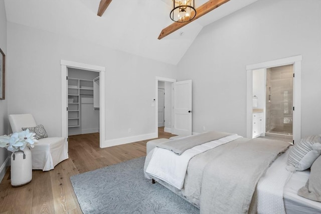 bedroom featuring wood finished floors, beamed ceiling, a walk in closet, and baseboards