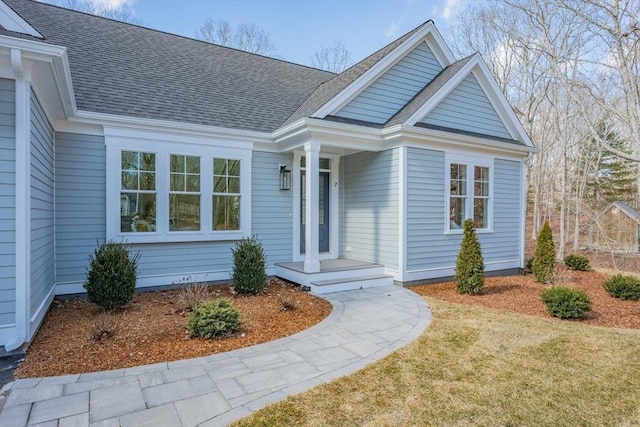 property entrance featuring a shingled roof and a lawn