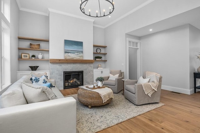 living area with baseboards, a tiled fireplace, ornamental molding, wood finished floors, and a chandelier