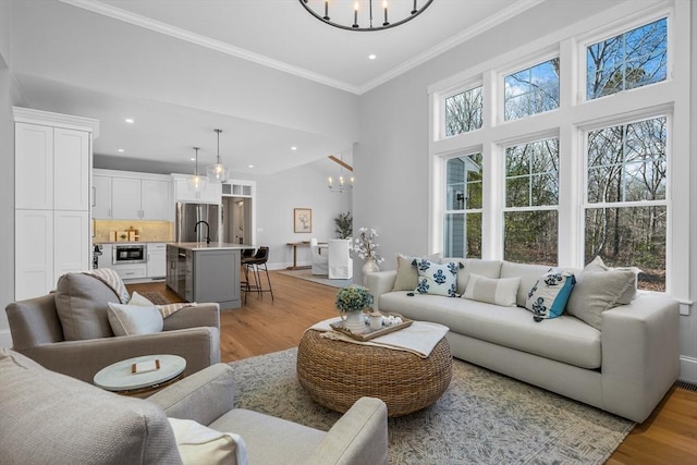 living area with crown molding, light wood finished floors, baseboards, and an inviting chandelier