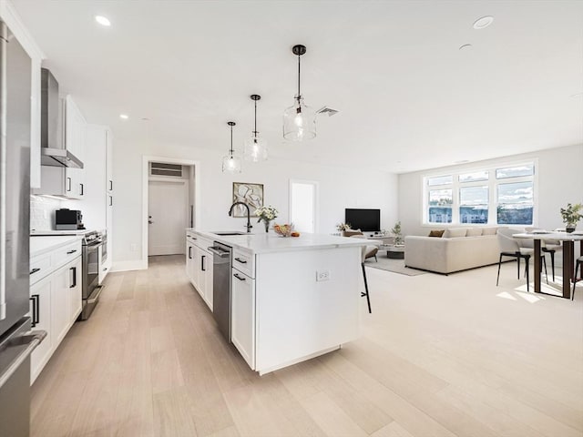 kitchen featuring stainless steel appliances, a kitchen island with sink, light wood finished floors, open floor plan, and light countertops