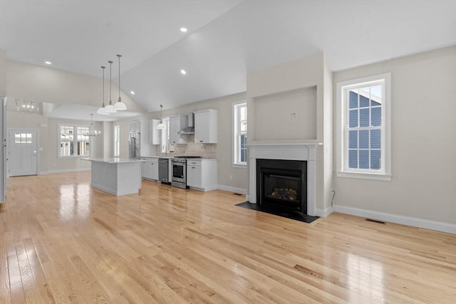 unfurnished living room featuring high vaulted ceiling, a chandelier, and light wood-type flooring