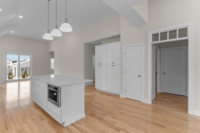 kitchen with white cabinetry, stainless steel oven, decorative light fixtures, a center island, and light wood-type flooring