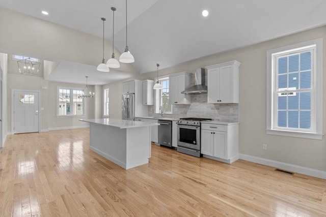 kitchen with pendant lighting, white cabinets, high end appliances, a notable chandelier, and wall chimney range hood