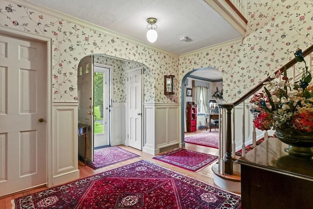 84 Englewood Rd, Longmeadow, MA 01106 - foyer with arched walkways, ornamental molding, wallpapered walls, a wainscoted wall, and light wood-style floors