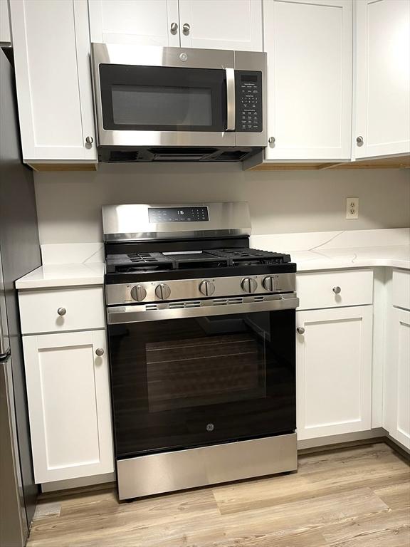 1550 Worcester Rd Unit 524, Framingham, MA 01702 - kitchen with stainless steel appliances, white cabinets, light wood-type flooring, and light stone countertops