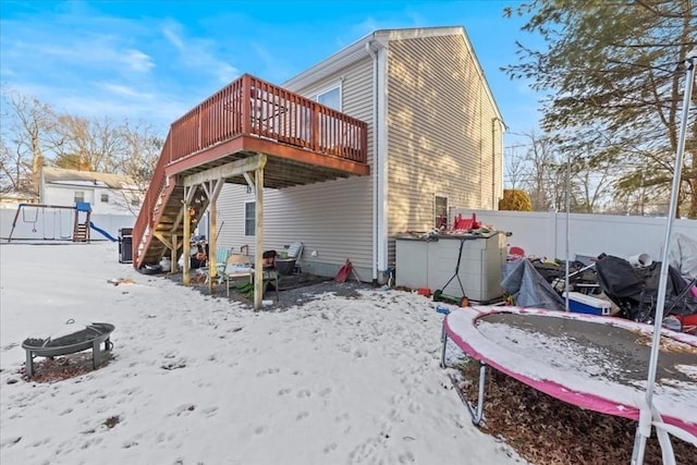 snow covered house with a deck, a trampoline, and an outdoor fire pit