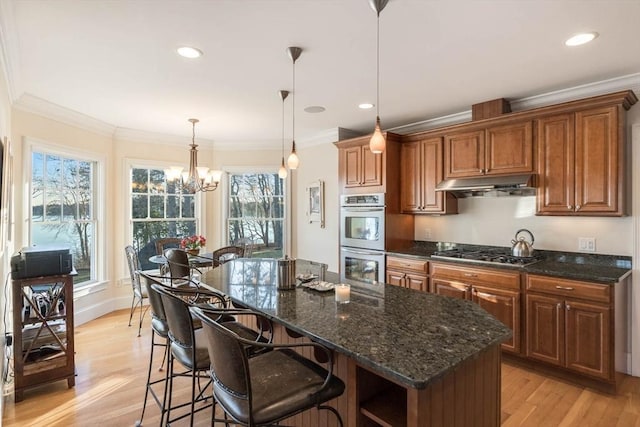 kitchen with crown molding, light hardwood / wood-style flooring, appliances with stainless steel finishes, a center island, and decorative light fixtures