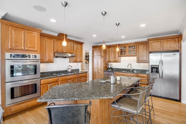 kitchen featuring a kitchen island, a breakfast bar, decorative light fixtures, stainless steel appliances, and light wood-type flooring