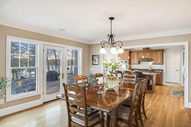 dining room featuring an inviting chandelier, ornamental molding, sink, and light hardwood / wood-style floors