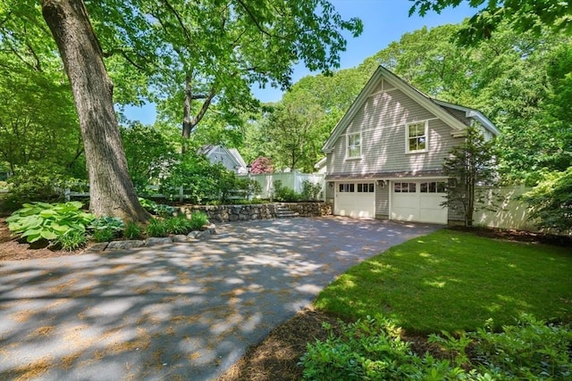 view of property exterior featuring a garage, fence, driveway, and a lawn