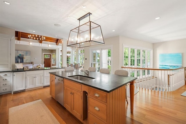 kitchen with stainless steel dishwasher, an island with sink, a sink, and white cabinetry