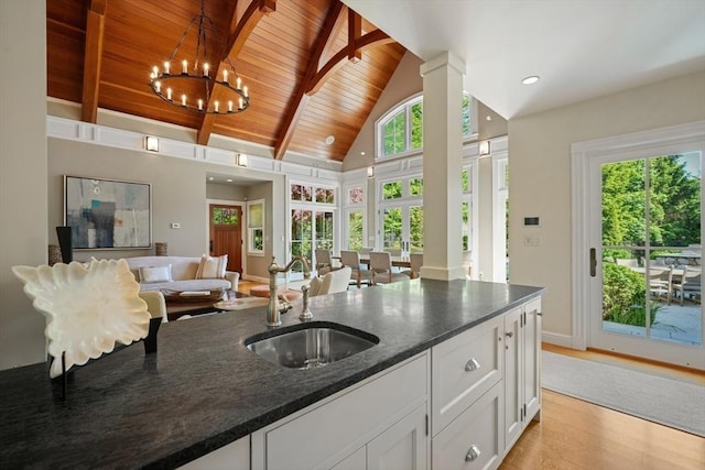 kitchen featuring a sink, white cabinets, open floor plan, dark stone countertops, and decorative light fixtures