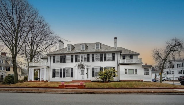 view of front facade featuring a front yard, a balcony, and a chimney