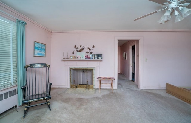 carpeted living area featuring a ceiling fan, baseboards, radiator heating unit, a tiled fireplace, and crown molding