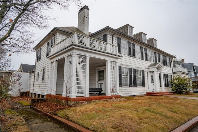 view of front facade with a front lawn, a chimney, and a balcony