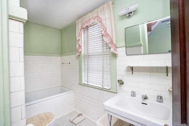 bathroom with tile walls, a tub to relax in, and a sink