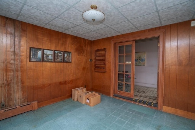 empty room featuring tile patterned floors, a baseboard heating unit, a paneled ceiling, and wood walls