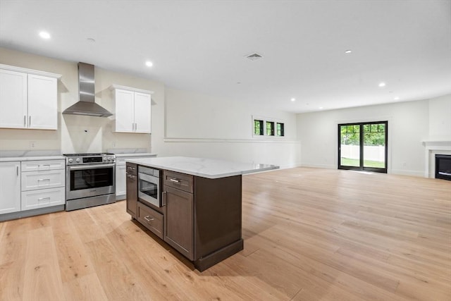 kitchen featuring white cabinets, wall chimney range hood, built in microwave, light hardwood / wood-style floors, and stainless steel range oven