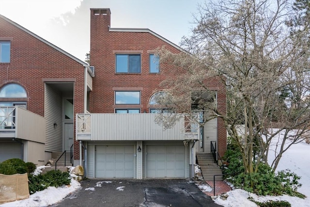 view of front of home featuring a balcony, brick siding, stairs, driveway, and a chimney