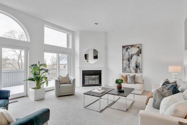 living area featuring a glass covered fireplace, a towering ceiling, and light colored carpet