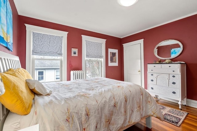 bedroom with radiator heating unit, crown molding, and wood finished floors