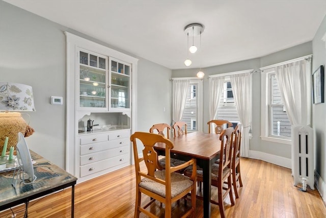 dining space with radiator heating unit, light wood-style flooring, and baseboards